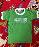 A green ringer t-shirt with white trim on the collar and cuffs, featuring a white graphic print on the front that reads '1986 Overstimulated Grown-UpS Running Club' 